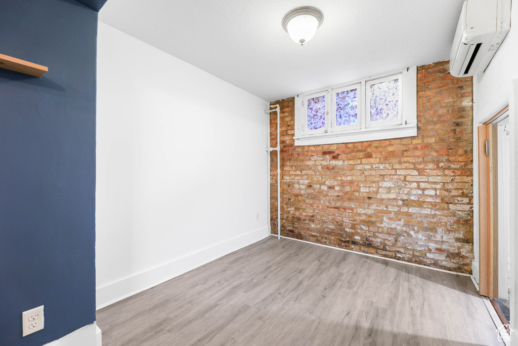 Unfurnished room featuring baseboards, brick wall, a wall unit AC, and wood finished floors