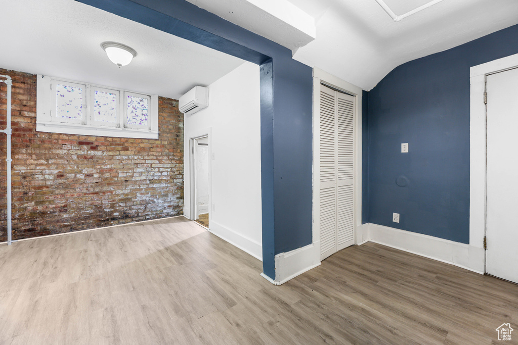 Interior space featuring baseboards, a wall mounted air conditioner, brick wall, and wood finished floors