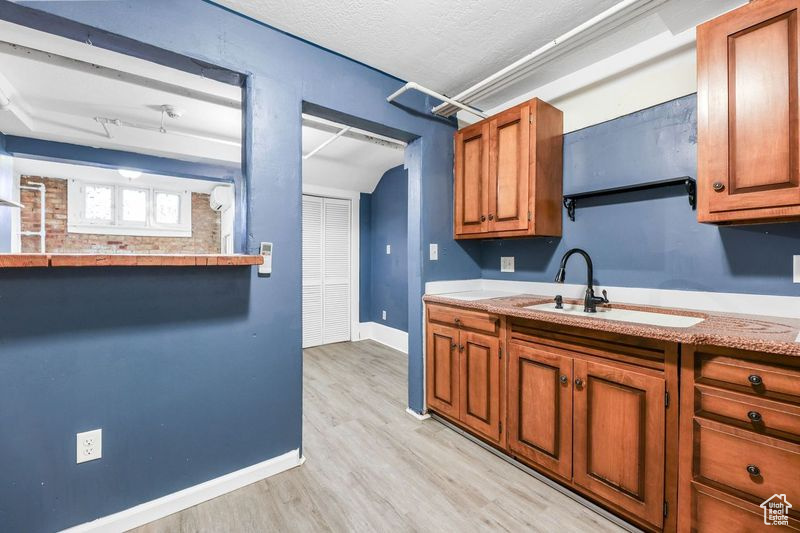 Kitchen featuring light wood-style floors, baseboards, light countertops, brown cabinets, and a sink