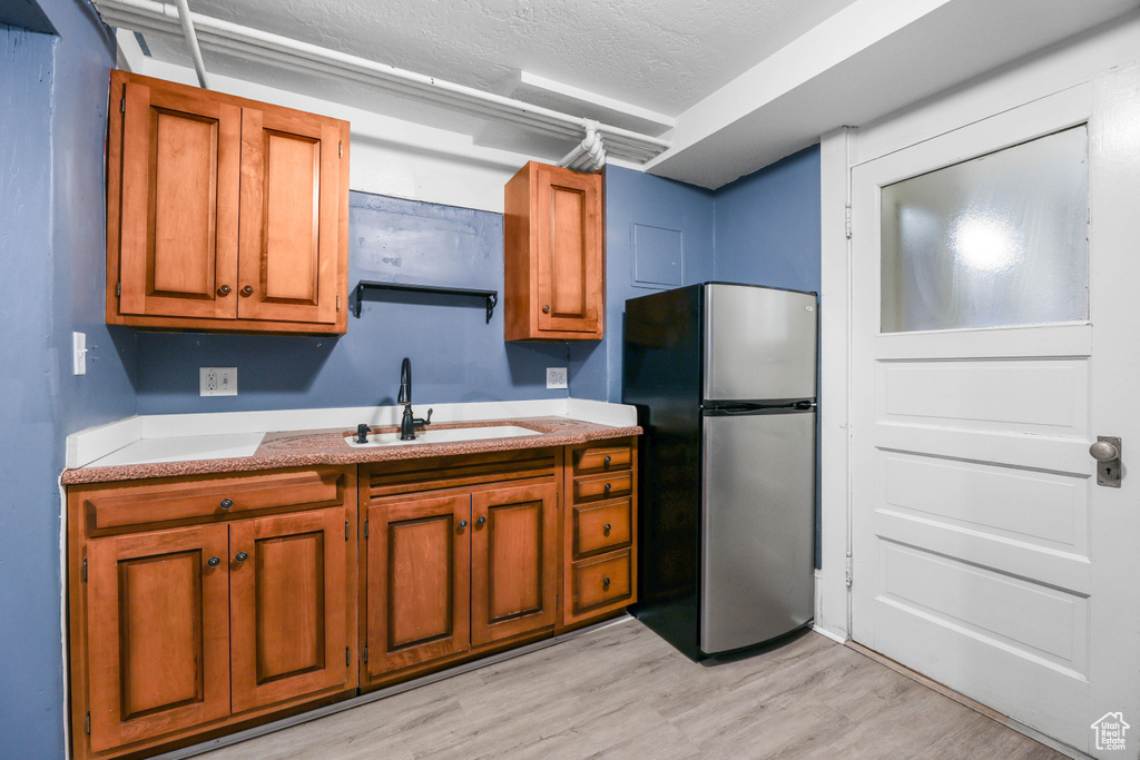 Kitchen featuring freestanding refrigerator, brown cabinetry, a sink, and light countertops