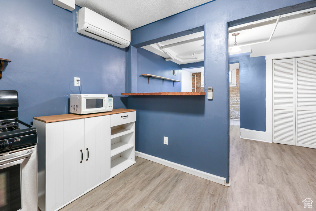 Kitchen with open shelves, an AC wall unit, gas range, wooden counters, and white microwave