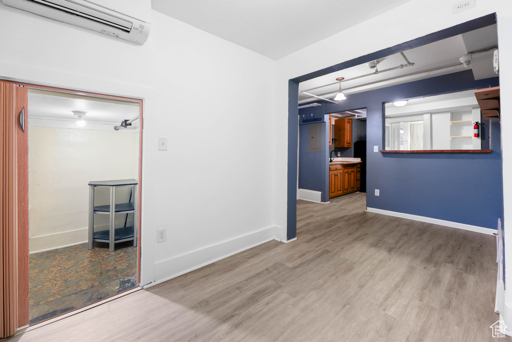 Empty room featuring baseboards, light wood-style floors, a sink, and a wall mounted air conditioner