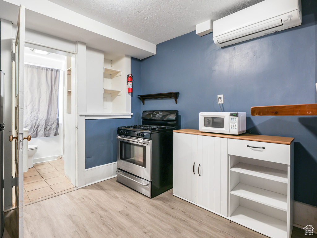 Kitchen with open shelves, light wood-style floors, an AC wall unit, white cabinetry, and stainless steel appliances
