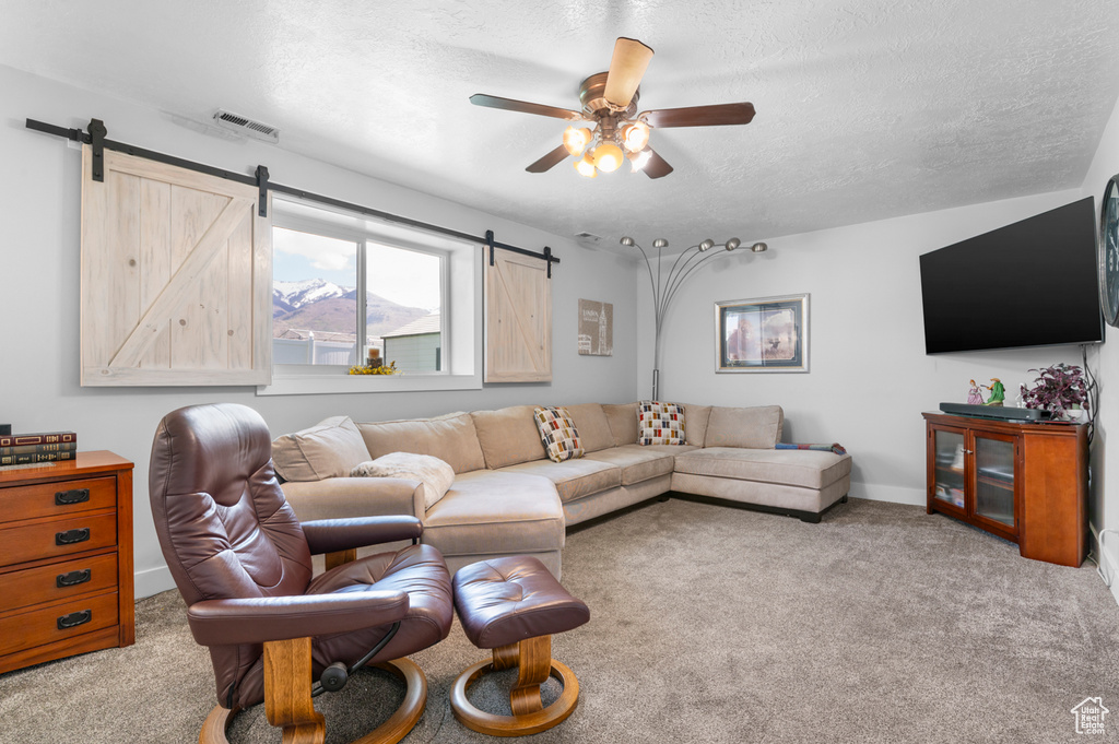Carpeted living room featuring visible vents, baseboards, ceiling fan, a barn door, and a textured ceiling