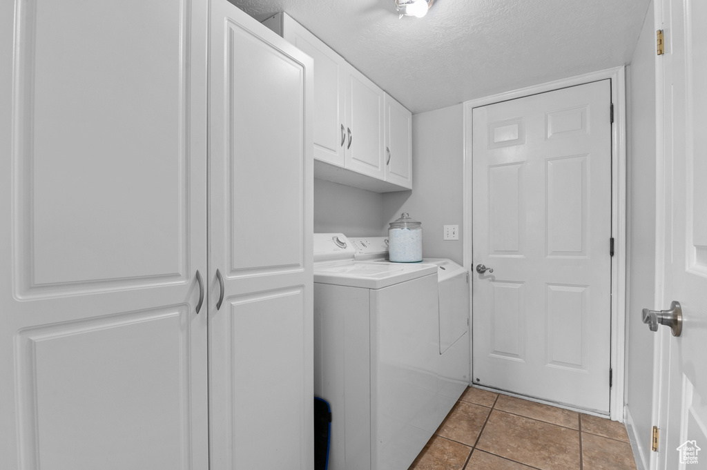 Washroom featuring a textured ceiling, light tile patterned flooring, cabinet space, and washer and dryer
