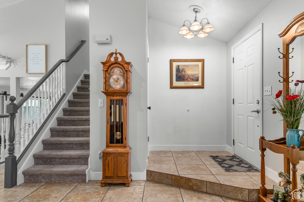 Foyer featuring a notable chandelier, stairs, baseboards, light tile patterned floors, and lofted ceiling