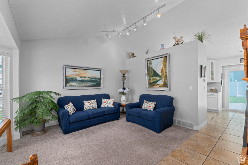 Living area featuring light tile patterned flooring, light carpet, baseboards, vaulted ceiling, and visible vents