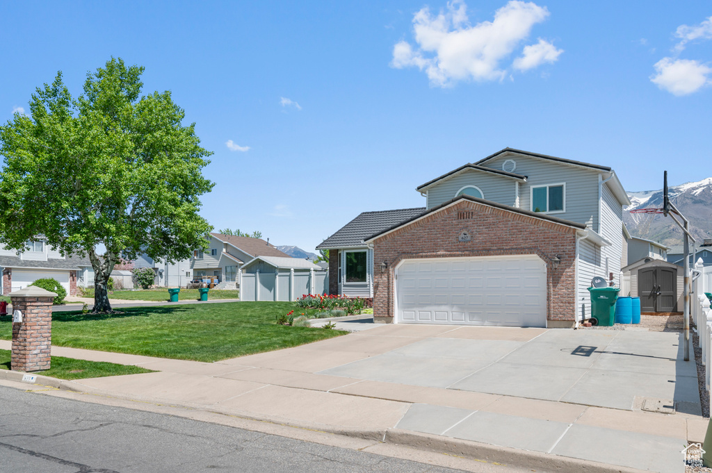 View of front of house featuring brick siding, a shed, a front lawn, concrete driveway, and an attached garage