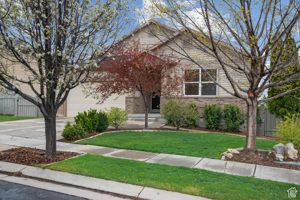 Obstructed view of property featuring a front yard, a garage, driveway, brick siding, and fence