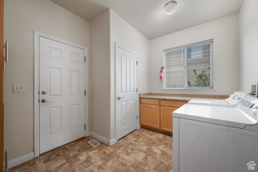 Clothes washing area with separate washer and dryer, cabinet space, stone finish flooring, baseboards, and visible vents