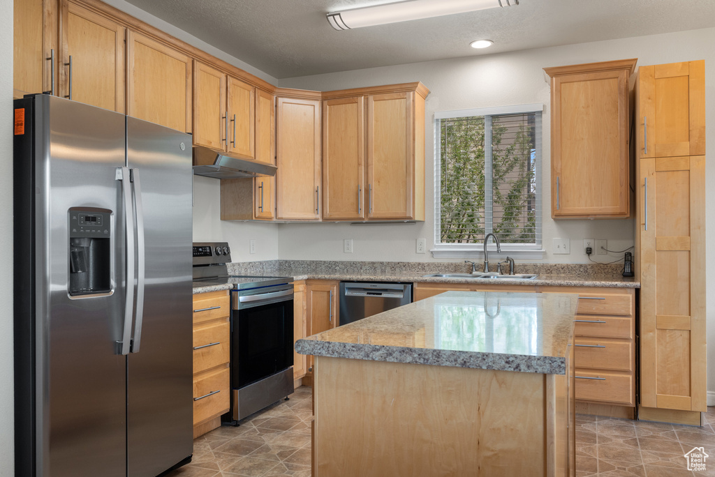 Kitchen with light brown cabinets, stainless steel appliances, under cabinet range hood, a sink, and a center island