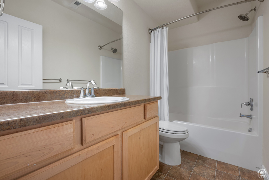 Full bathroom with stone finish floor, shower / tub combo, visible vents, toilet, and vanity