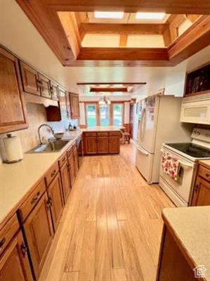 Kitchen featuring a sink, white appliances, light countertops, brown cabinetry, and light wood-type flooring