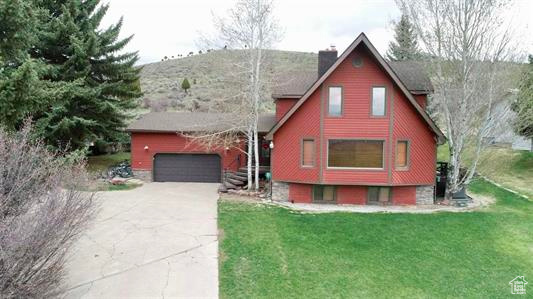 Chalet / cabin with concrete driveway, a garage, a chimney, and a front lawn