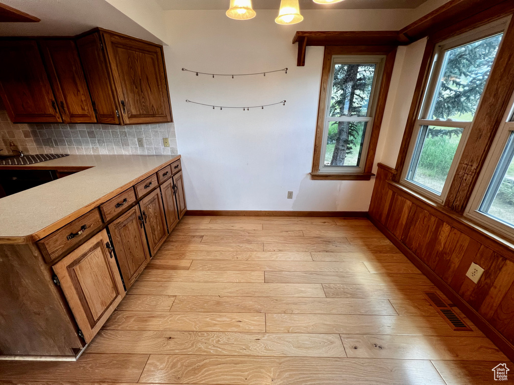 Kitchen featuring light wood-style flooring, decorative backsplash, light countertops, brown cabinets, and wainscoting