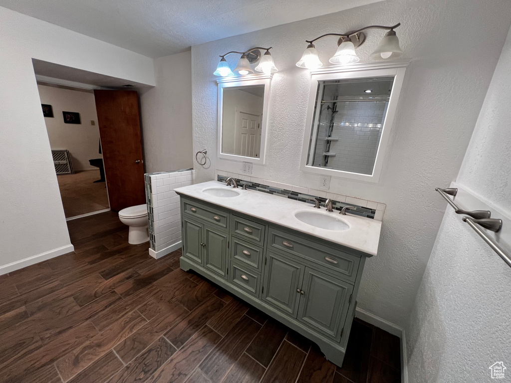 Full bathroom with wood finished floors, toilet, double vanity, a textured wall, and baseboards