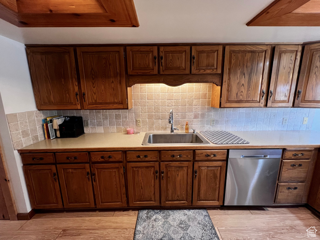 Kitchen with dishwasher, a sink, light countertops, decorative backsplash, and light wood finished floors