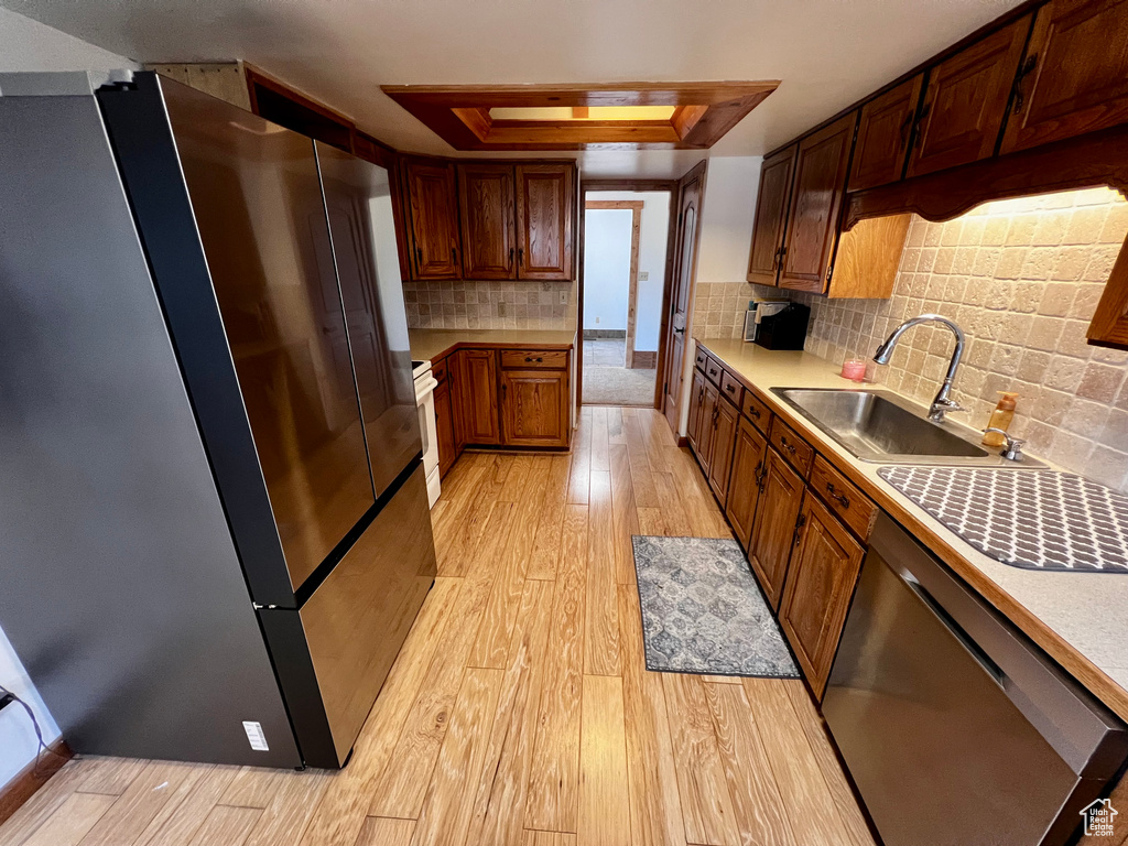 Kitchen featuring stainless steel appliances, a sink, a raised ceiling, light wood-type flooring, and light countertops