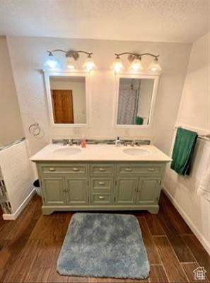 Bathroom featuring double vanity, baseboards, wood finished floors, and a sink