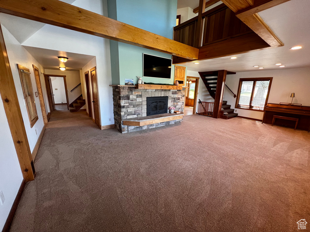 Unfurnished living room with stairs, light colored carpet, a stone fireplace, baseboards, and recessed lighting
