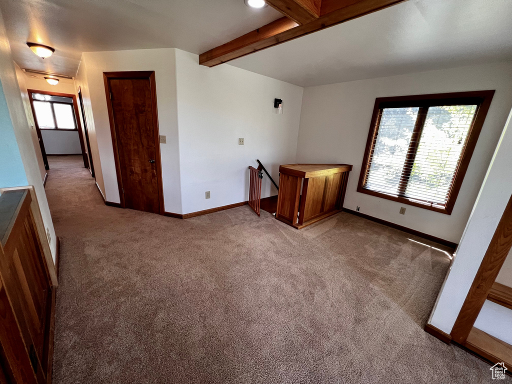 Spare room featuring carpet floors, beam ceiling, and baseboards