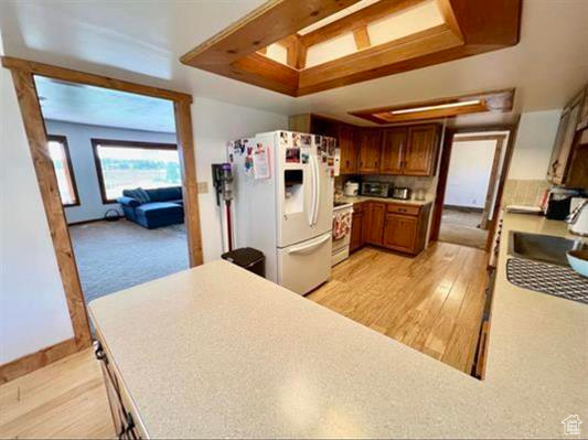 Kitchen featuring electric range, light wood finished floors, light countertops, brown cabinetry, and white fridge with ice dispenser