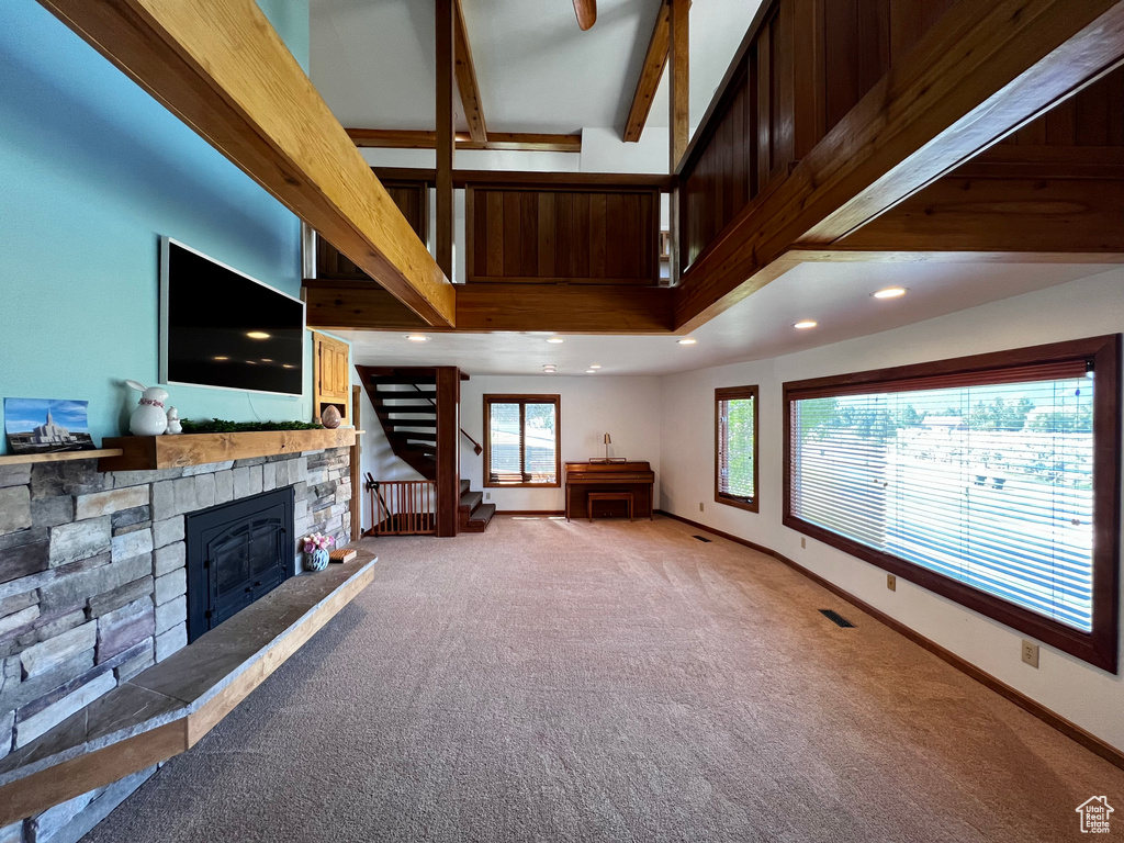 Unfurnished living room featuring carpet floors, stairs, beamed ceiling, a stone fireplace, and recessed lighting