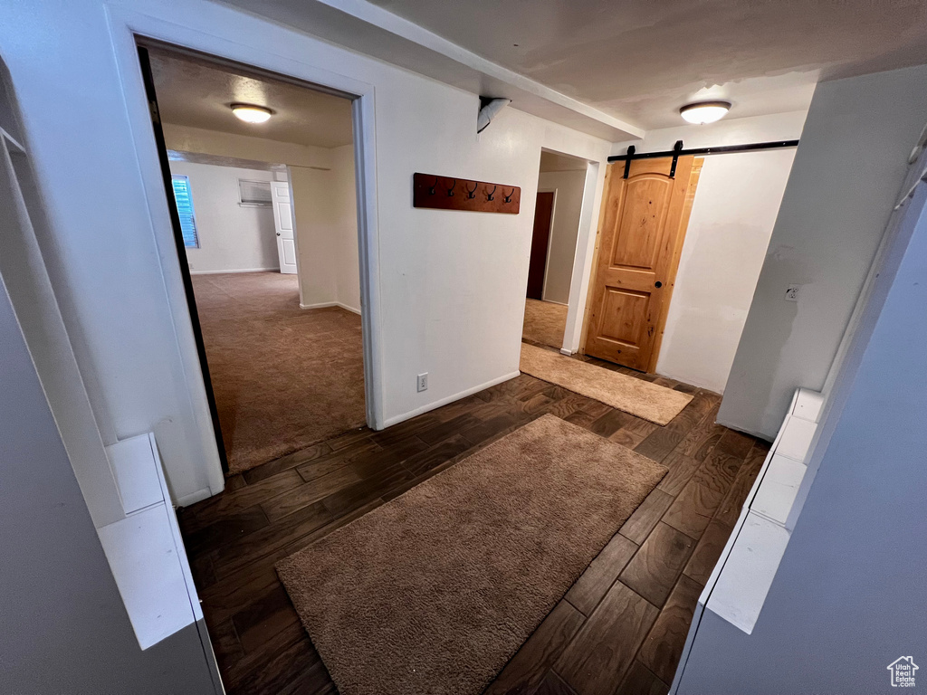 Corridor featuring a barn door, dark wood-type flooring, and baseboards
