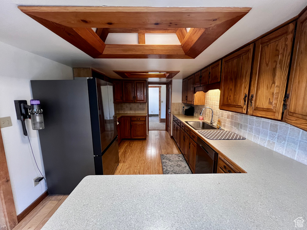 Kitchen featuring freestanding refrigerator, a sink, dishwashing machine, a raised ceiling, and light wood-style floors