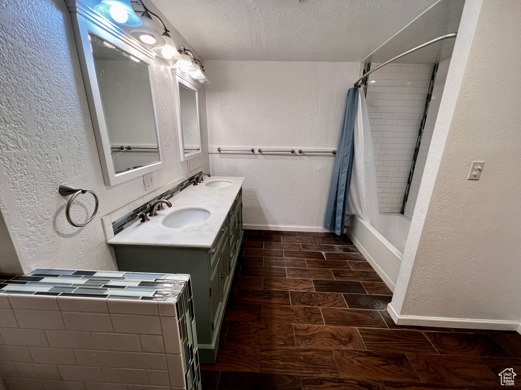 Bathroom with a textured wall, wood finish floors, a textured ceiling, double vanity, and baseboards