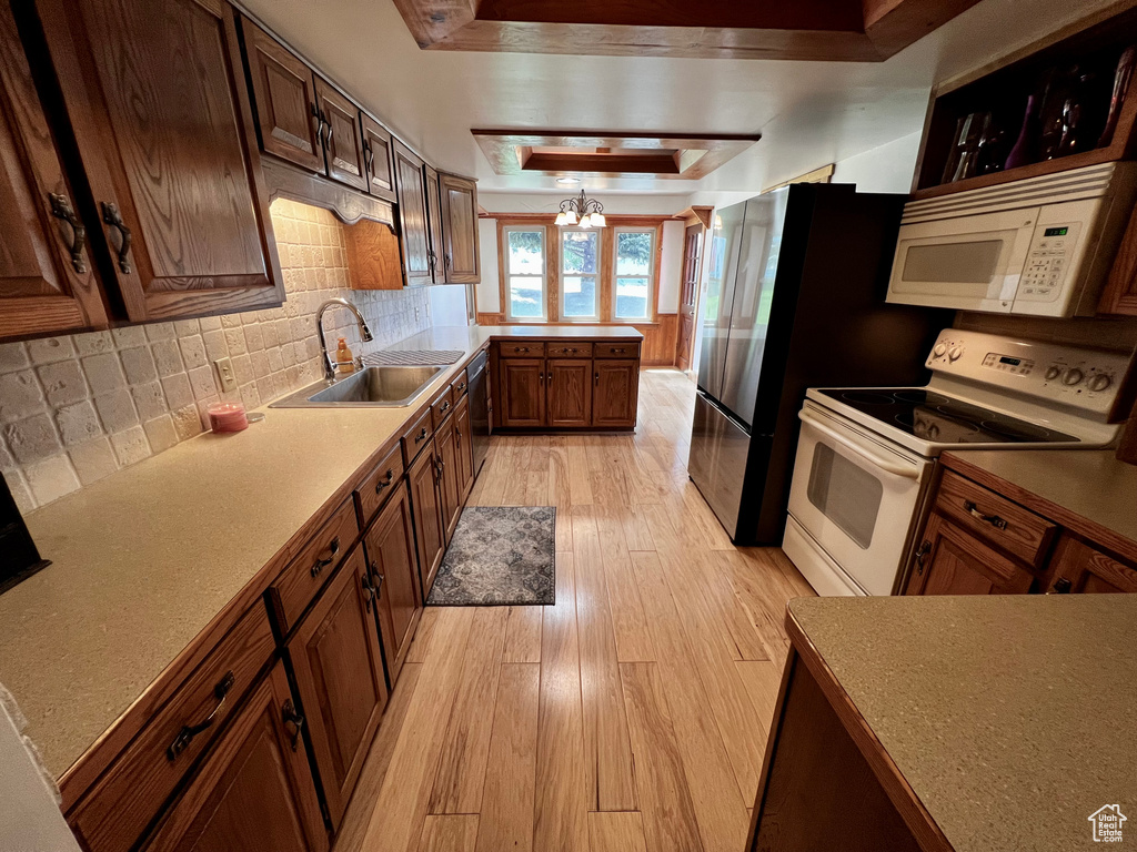 Kitchen featuring white appliances, a tray ceiling, a sink, light wood-style floors, and tasteful backsplash