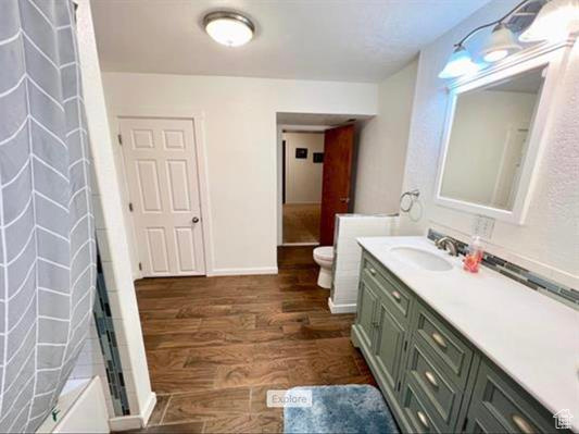 Full bath with vanity, toilet, baseboards, wood finished floors, and a shower with curtain