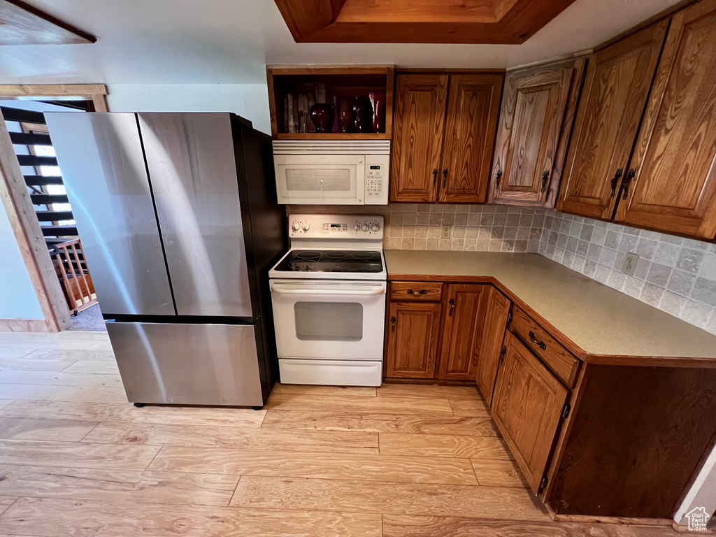 Kitchen featuring white appliances, brown cabinetry, tasteful backsplash, and light wood finished floors
