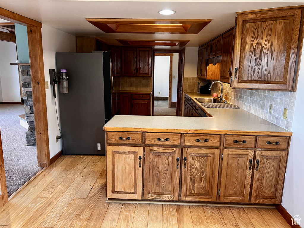 Kitchen featuring freestanding refrigerator, a sink, light wood finished floors, a peninsula, and light countertops
