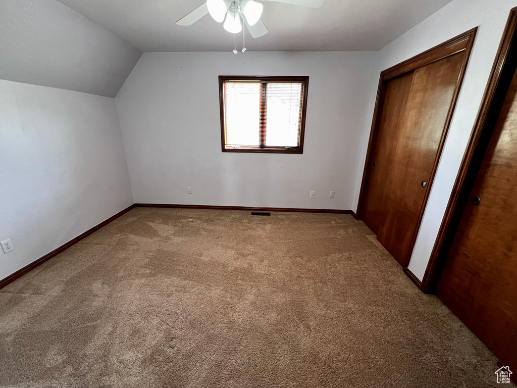 Unfurnished bedroom with carpet floors, vaulted ceiling, baseboards, a ceiling fan, and two closets