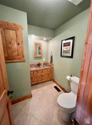 Half bathroom with baseboards, tile patterned floors, toilet, and vanity
