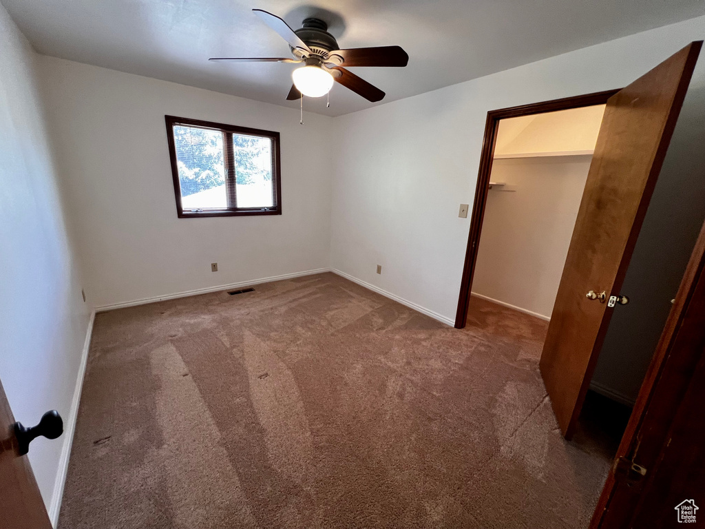 Unfurnished bedroom featuring carpet floors, baseboards, ceiling fan, and a walk in closet