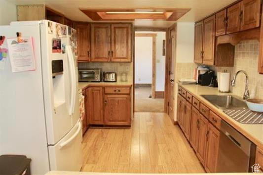 Kitchen with brown cabinets, a sink, white fridge with ice dispenser, light wood-type flooring, and stainless steel dishwasher