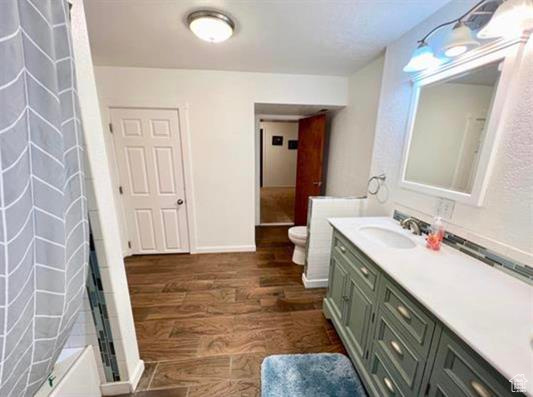 Bathroom with vanity, toilet, baseboards, wood finished floors, and curtained shower