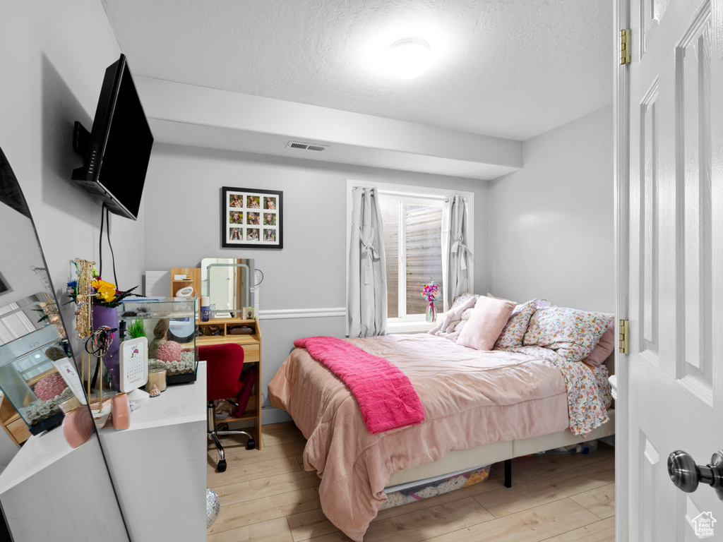 Bedroom with light wood finished floors, a textured ceiling, and visible vents