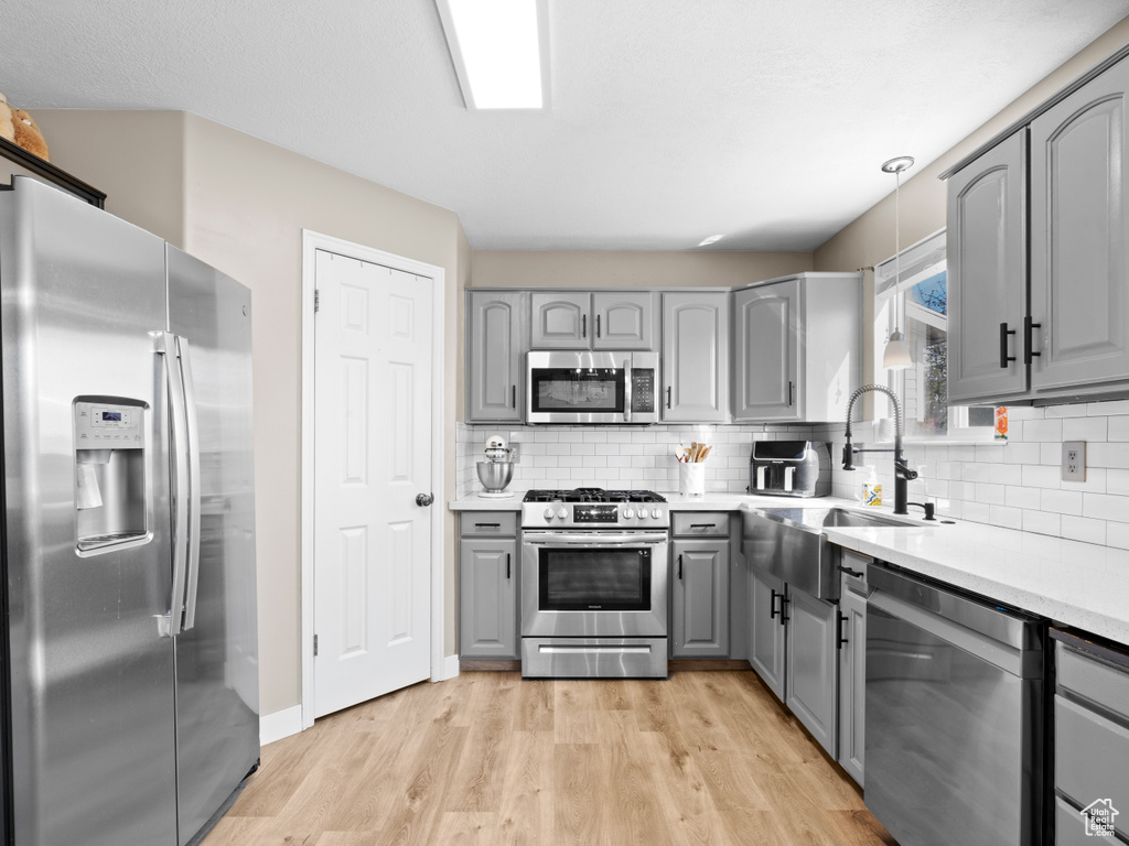Kitchen featuring gray cabinets, backsplash, light wood-type flooring, a sink, and stainless steel appliances