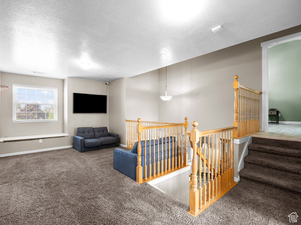 Interior space featuring carpet flooring, a textured ceiling, an upstairs landing, and baseboards
