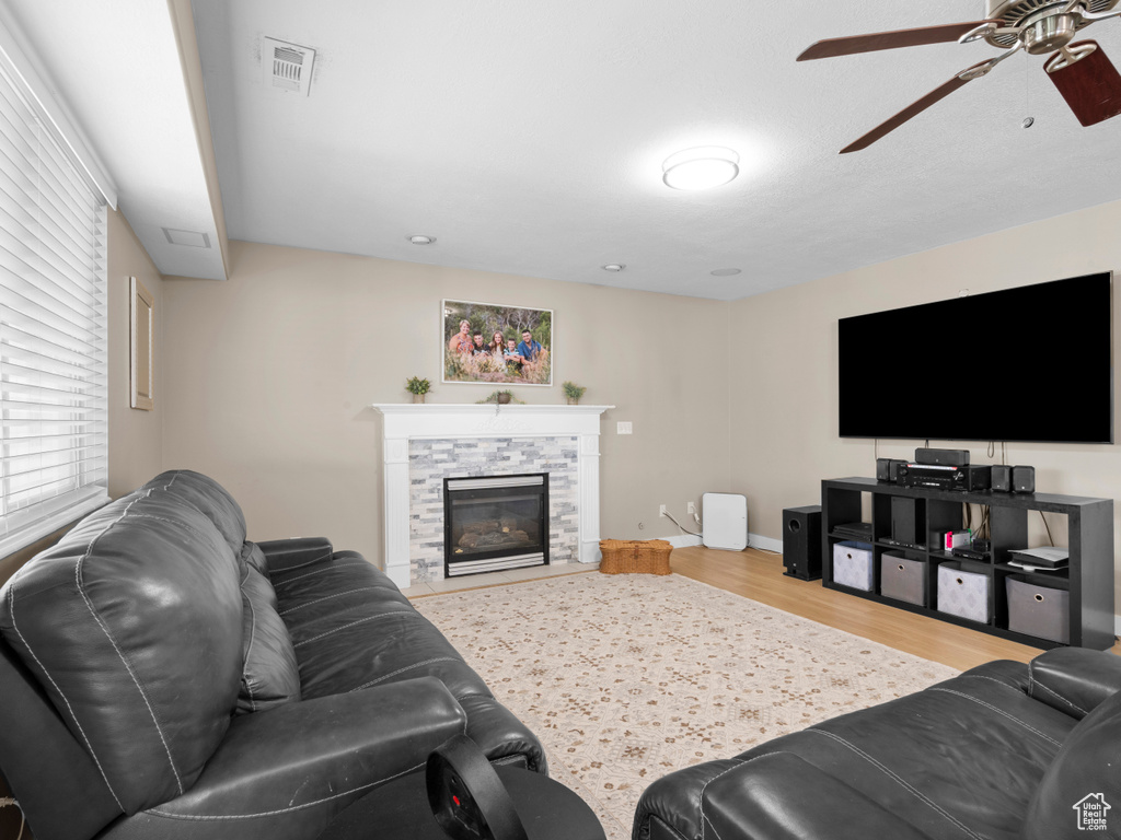 Living room with a stone fireplace, a ceiling fan, baseboards, wood finished floors, and visible vents