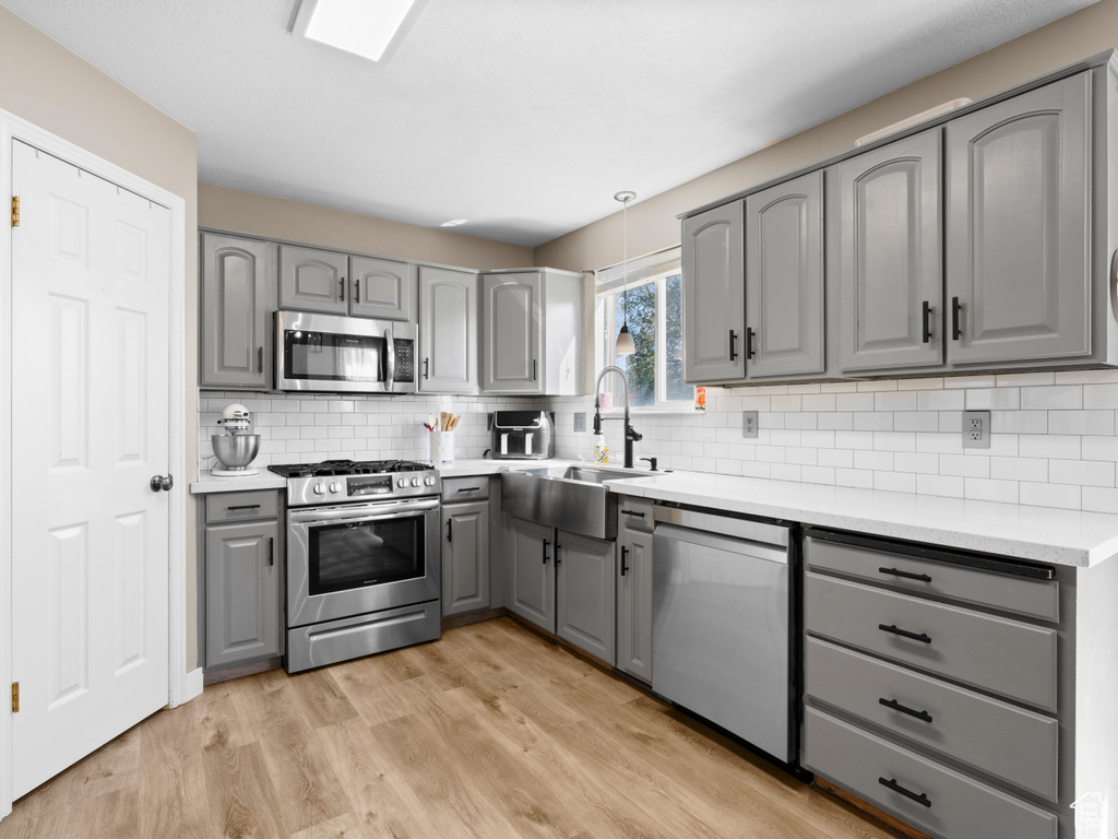 Kitchen featuring gray cabinets, tasteful backsplash, light wood-type flooring, a sink, and stainless steel appliances