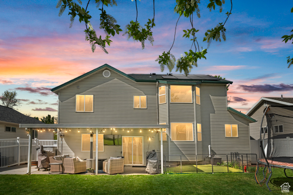 Back of property at dusk featuring an outdoor hangout area, a trampoline, a fenced backyard, and a patio
