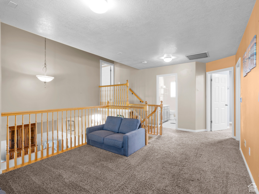 Living area with a textured ceiling, visible vents, baseboards, an upstairs landing, and carpet flooring
