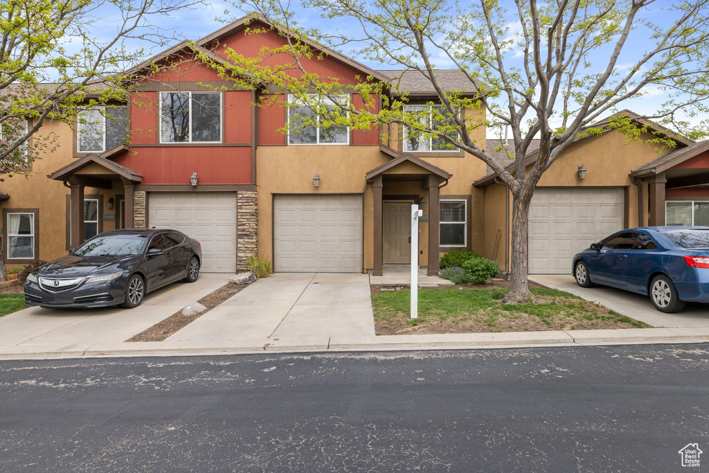 View of front of home with an attached garage, stucco siding, driveway, and stone siding