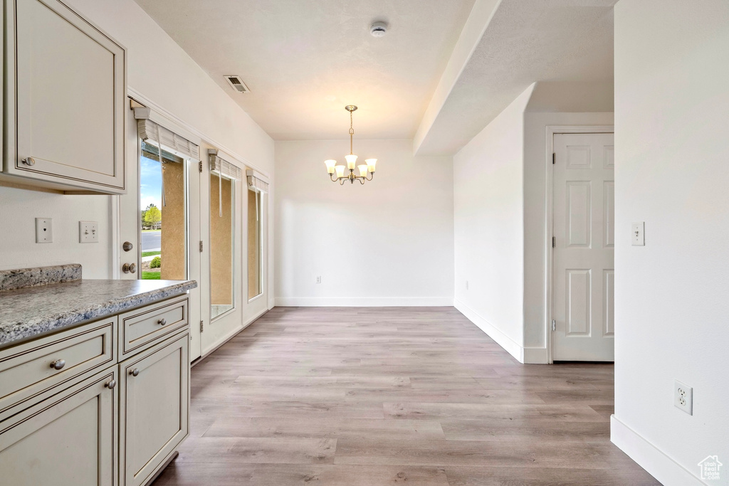 Unfurnished dining area with baseboards, a notable chandelier, visible vents, and light wood-style floors