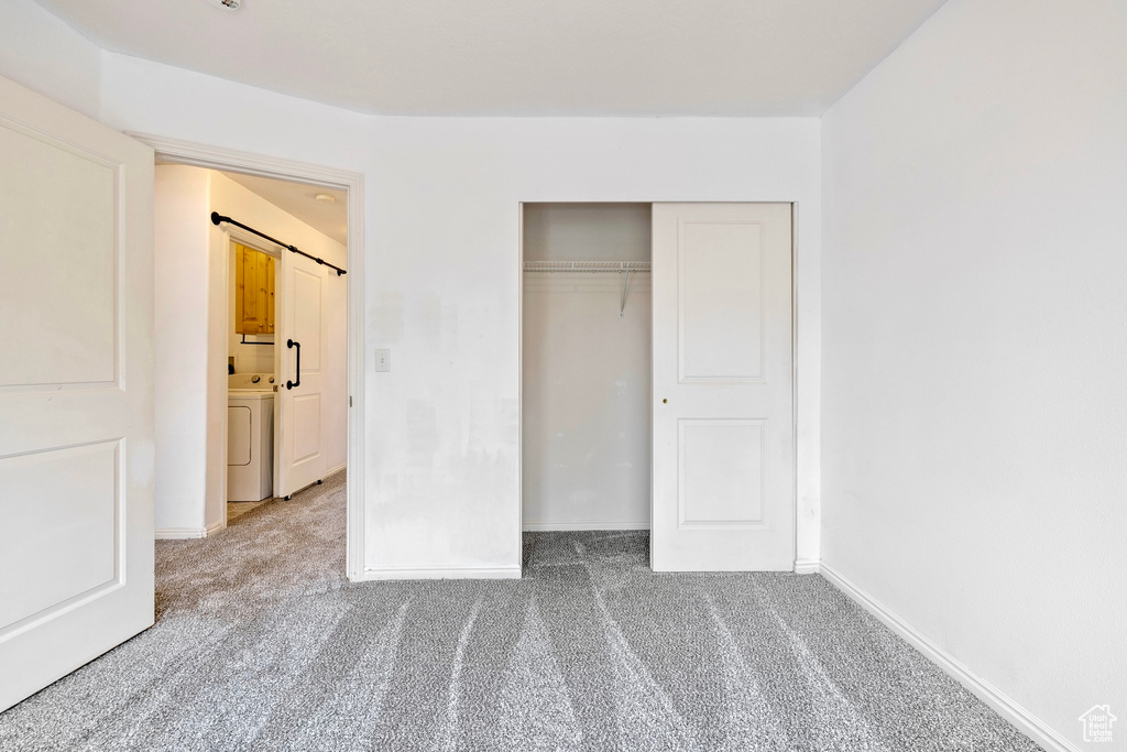 Unfurnished bedroom featuring a closet, baseboards, carpet flooring, and a barn door