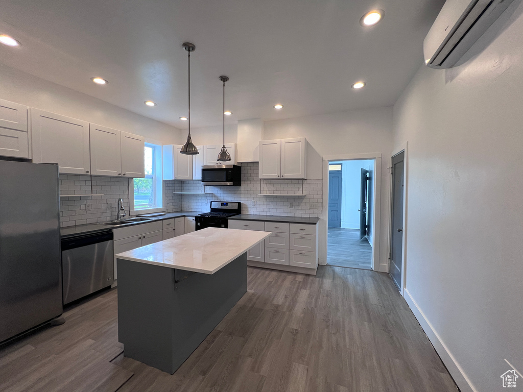 Kitchen featuring dark wood-style flooring, a wall mounted AC, tasteful backsplash, a sink, and appliances with stainless steel finishes